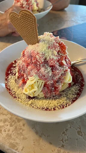 Spaghetti-Eis mit roter Sauce, weißer Schokolade und Eiswaffel auf einem Teller